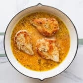 Adding the chicken breast back to the skillet with the pan sauce.