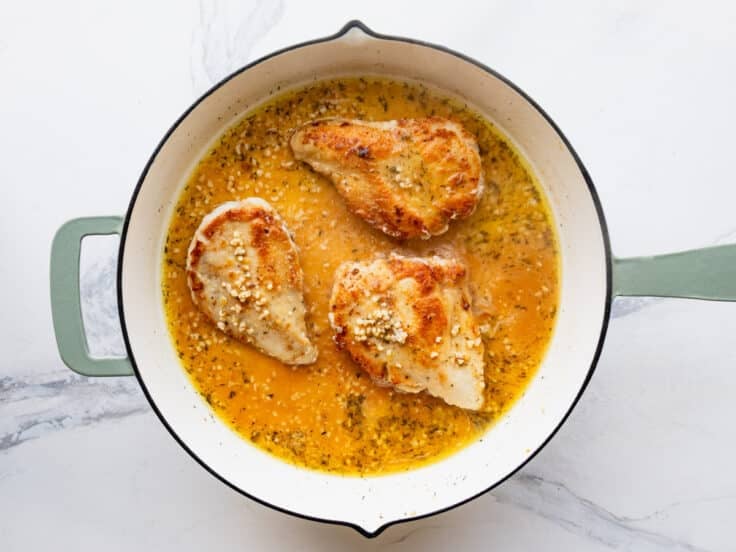 Adding the chicken breast back to the skillet with the pan sauce.
