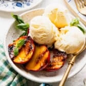 Square shot of a bowl of grilled peaches served with vanilla ice cream and garnished with fresh basil.