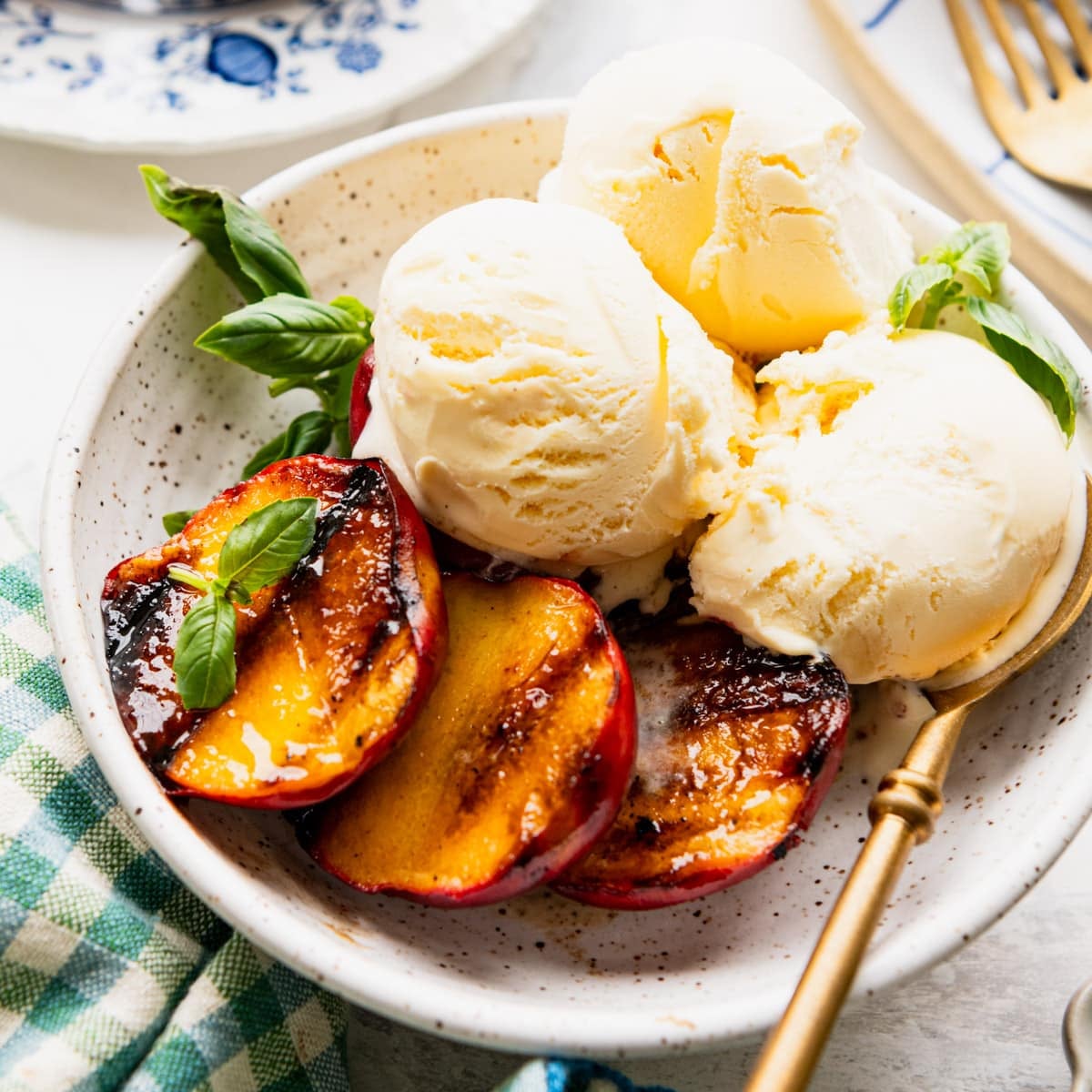 Square shot of a bowl of grilled peaches served with vanilla ice cream and garnished with fresh basil.