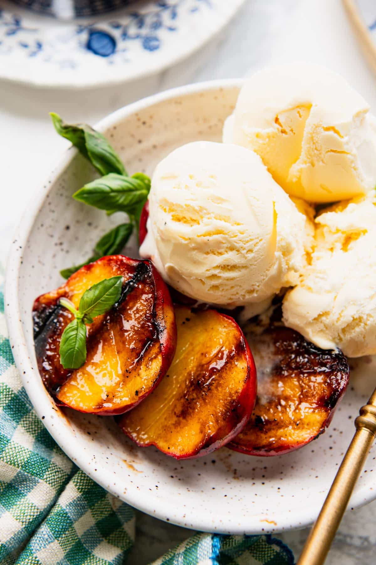 Bowl of grilled peaches served with vanilla ice cream and garnished with fresh basil.