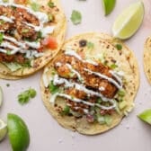 Horizontal overhead image of shrimp tacos with toppings on a white surface.