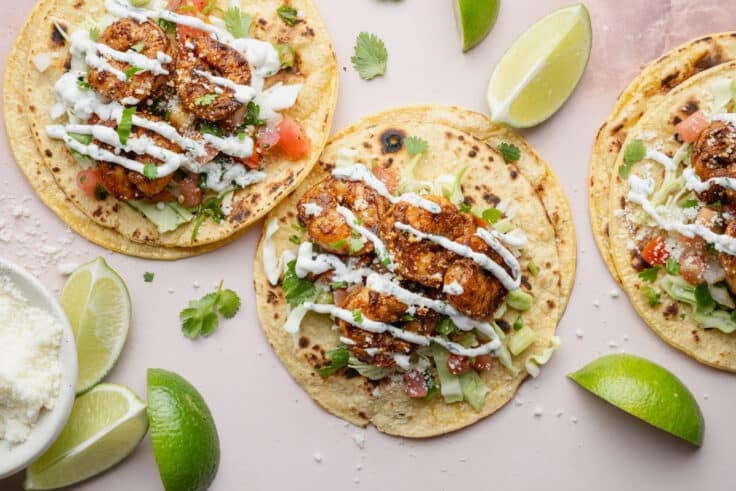 Horizontal overhead image of shrimp tacos with toppings on a white surface.