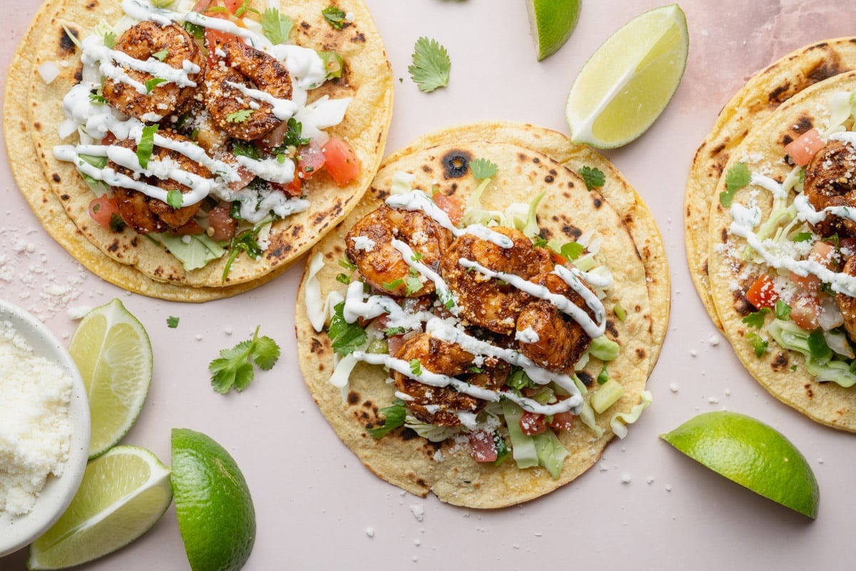 Horizontal overhead image of shrimp tacos with toppings on a white surface.