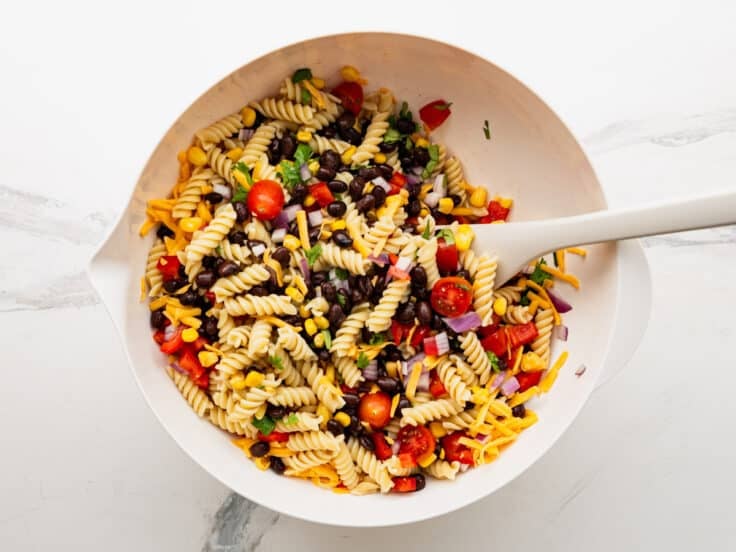 Adding corn, beans, and other ingredients to the cooked pasta.