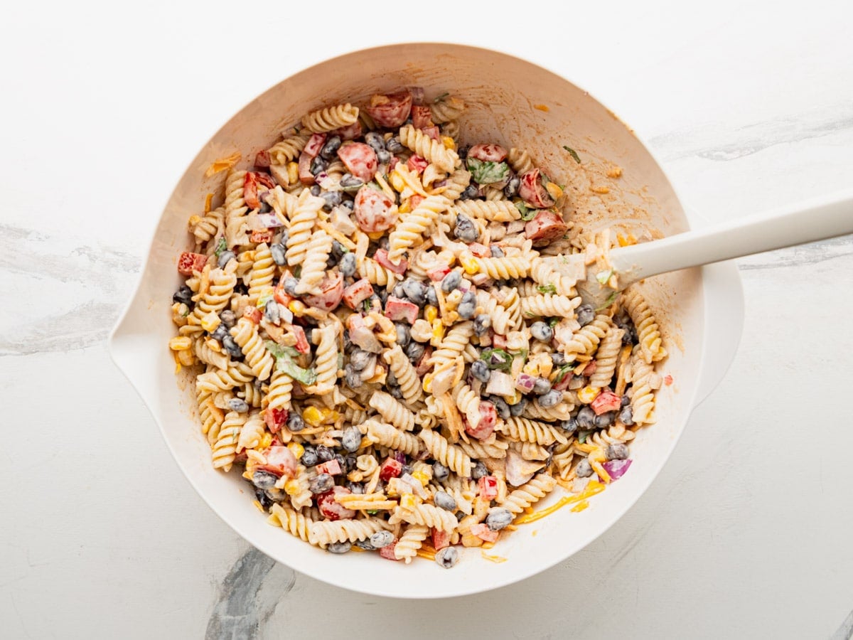 Combining the pasta salad ingredients with the dressing.