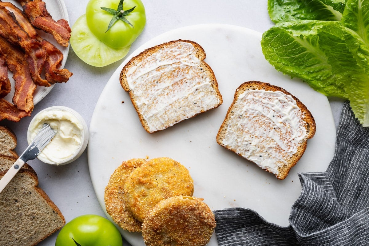 Spreading mayo on two slices of toasted bread.