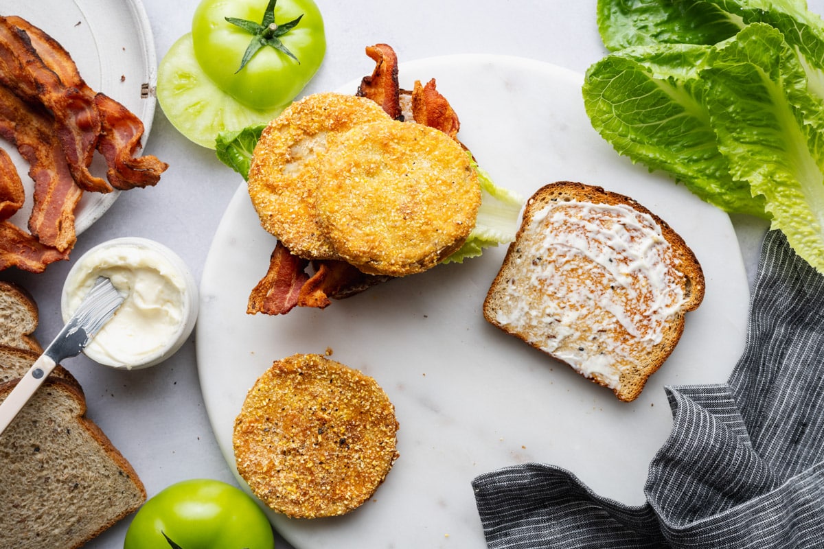 Assembling the fried green tomato BLT sandwich before adding the final piece of bread on top.