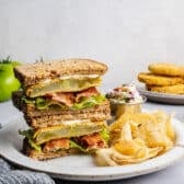 Horizontal side shot of two halves of a Southern fried green tomato BLT sandwich stacked on a plate.