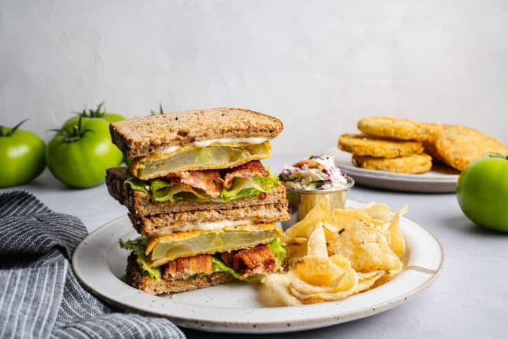 Horizontal side shot of two halves of a Southern fried green tomato BLT sandwich stacked on a plate.