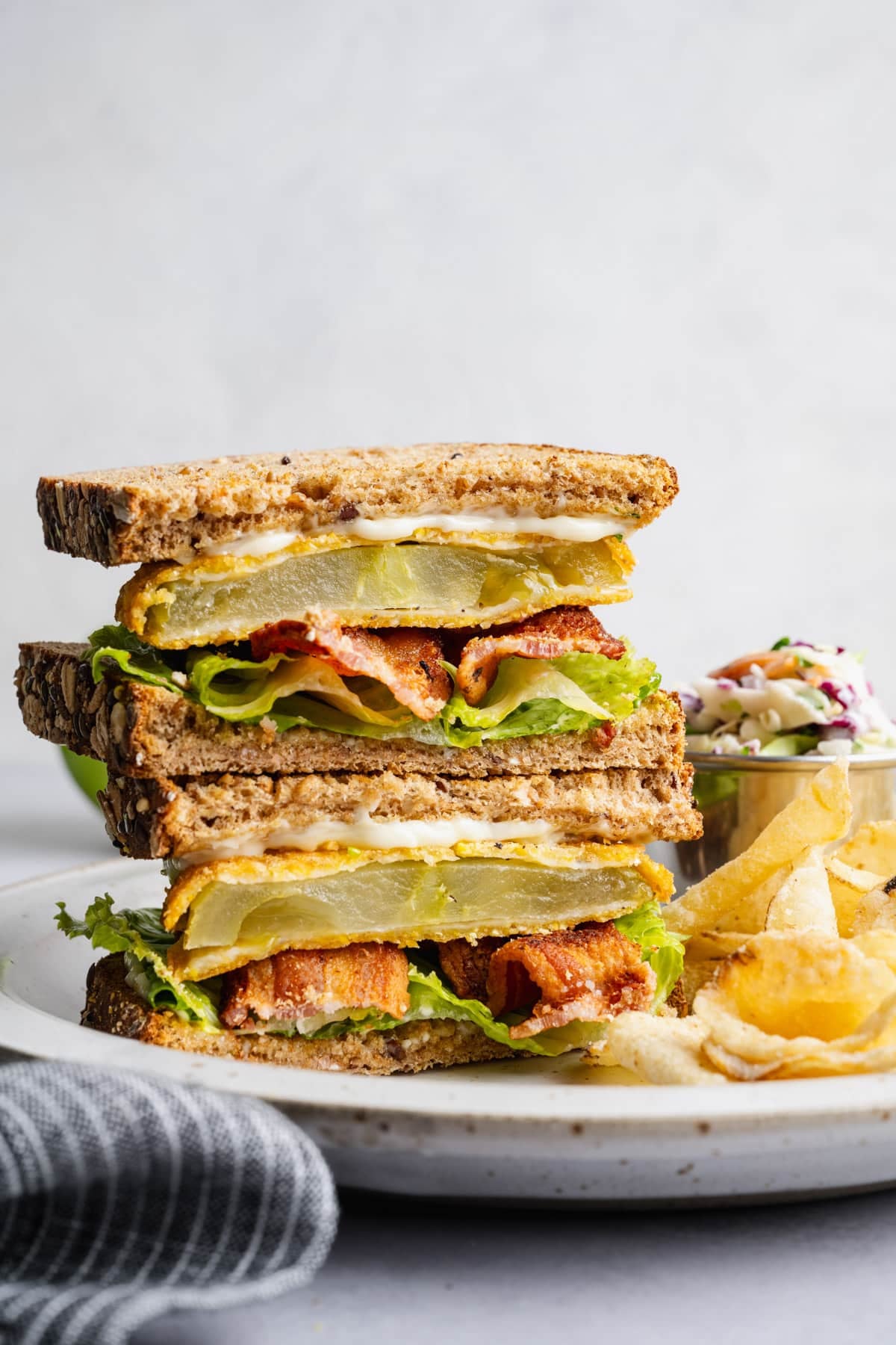 Side shot of two halves of a Southern fried green tomato BLT sandwich stacked on a plate.