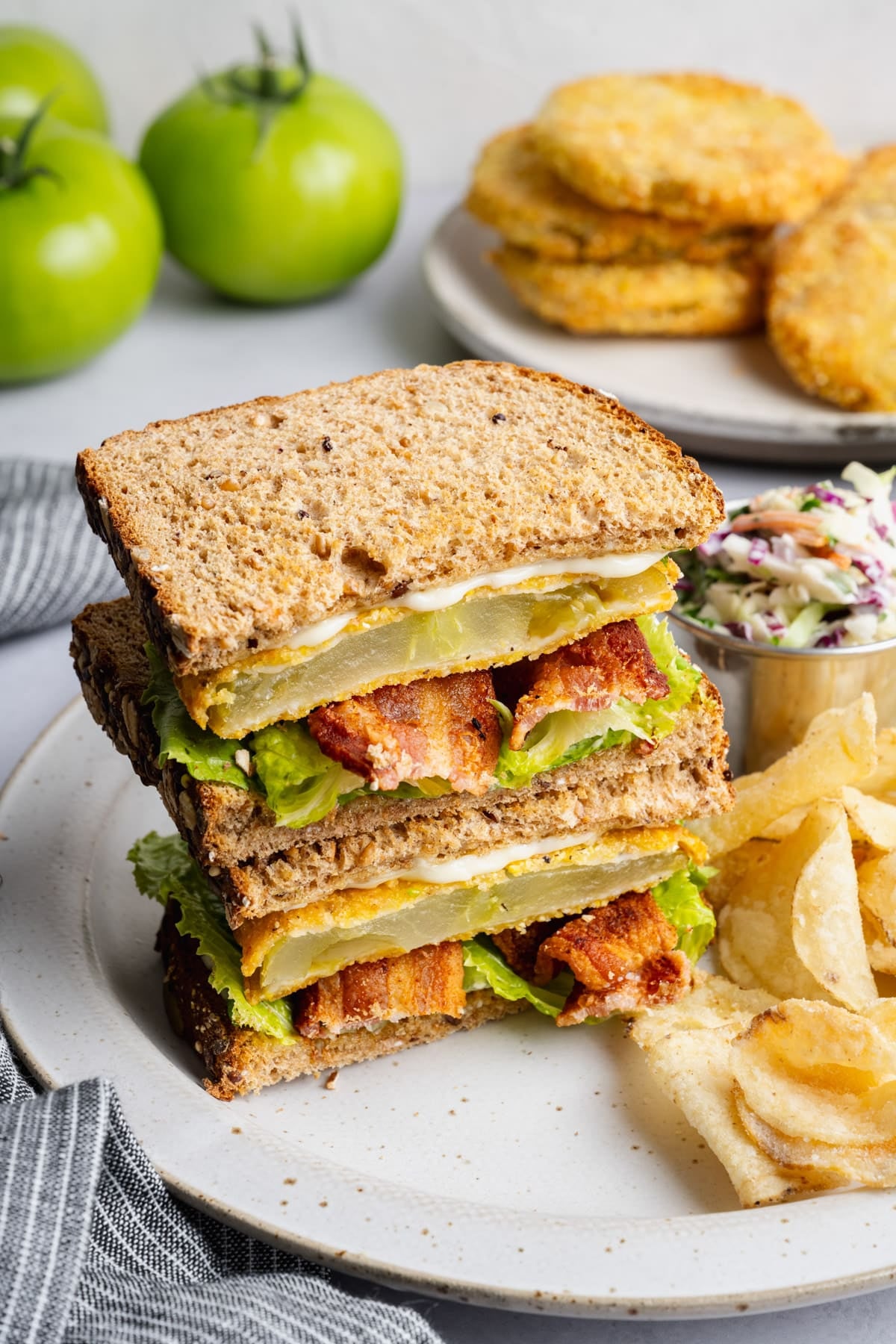 Angle shot from above of two halves of a Southern fried green tomato BLT sandwich stacked on a plate.