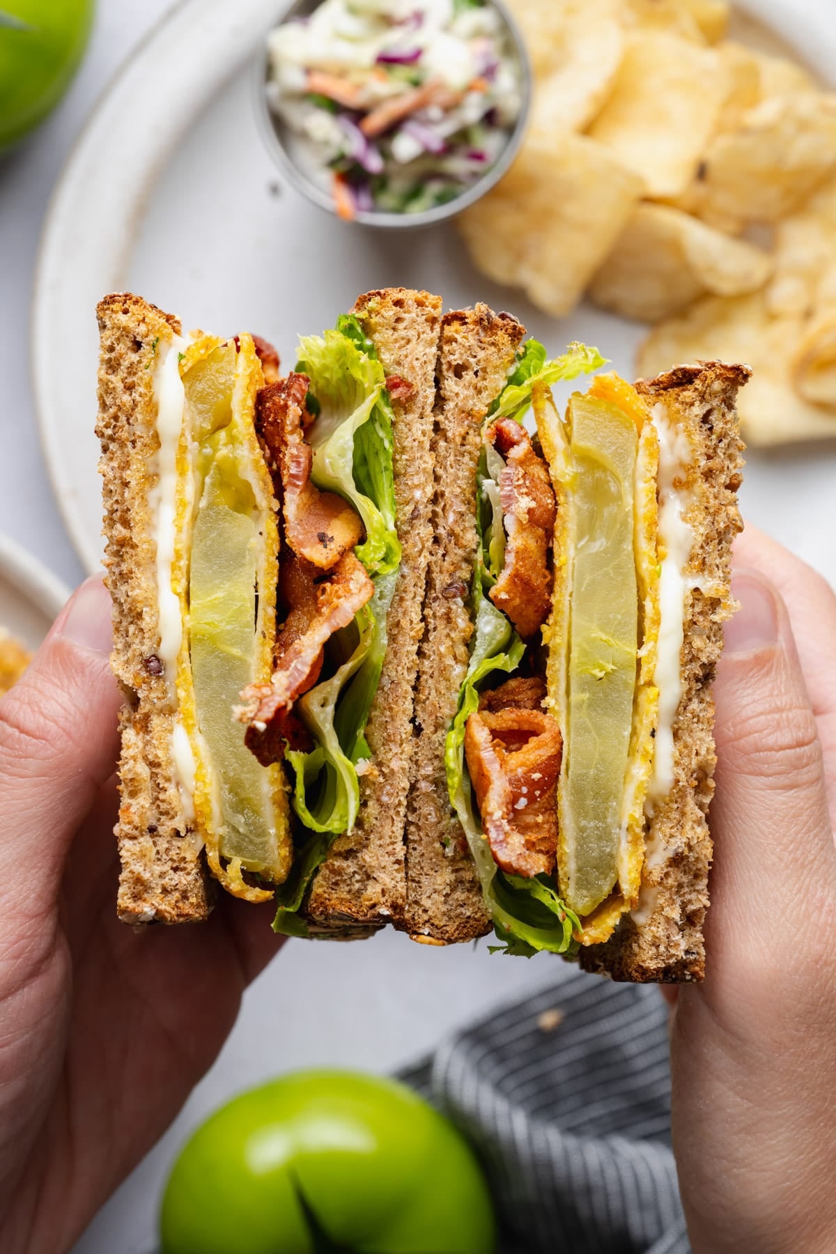 Hands holding two halves of a fried green tomato BLT sandwich.