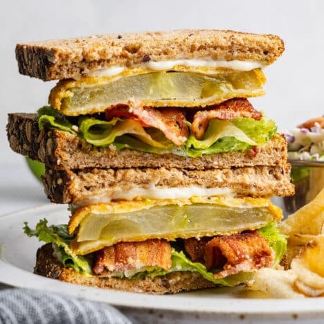 Square side shot of two halves of a Southern fried green tomato BLT sandwich stacked on a plate.