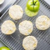 Breaded green tomatoes drying on a wire rack before frying.