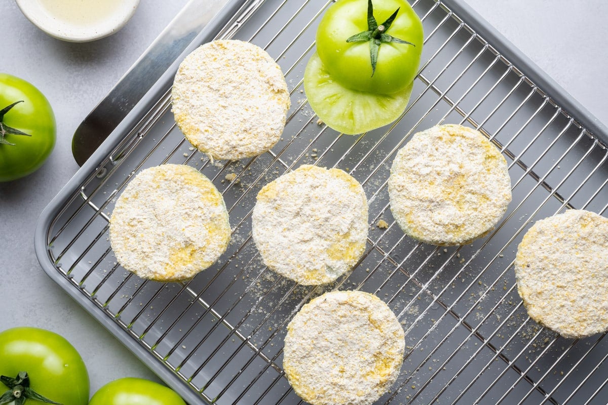 Breaded green tomatoes drying on a wire rack before frying.