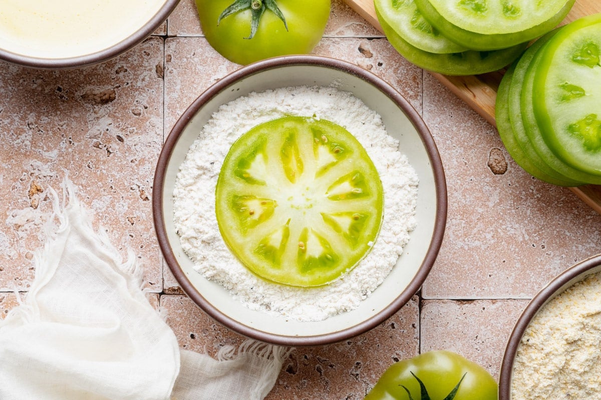 Dredging a green tomato slice in the flour.