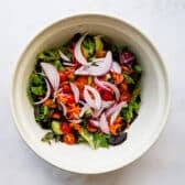 Adding additional veggies and ingredients to the bowl with the greens.