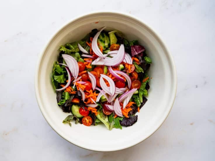 Adding additional veggies and ingredients to the bowl with the greens.