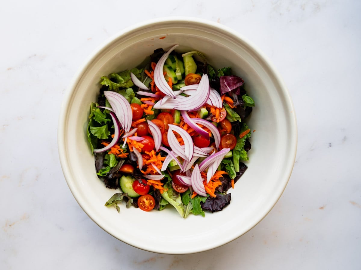 Adding additional veggies and ingredients to the bowl with the greens.