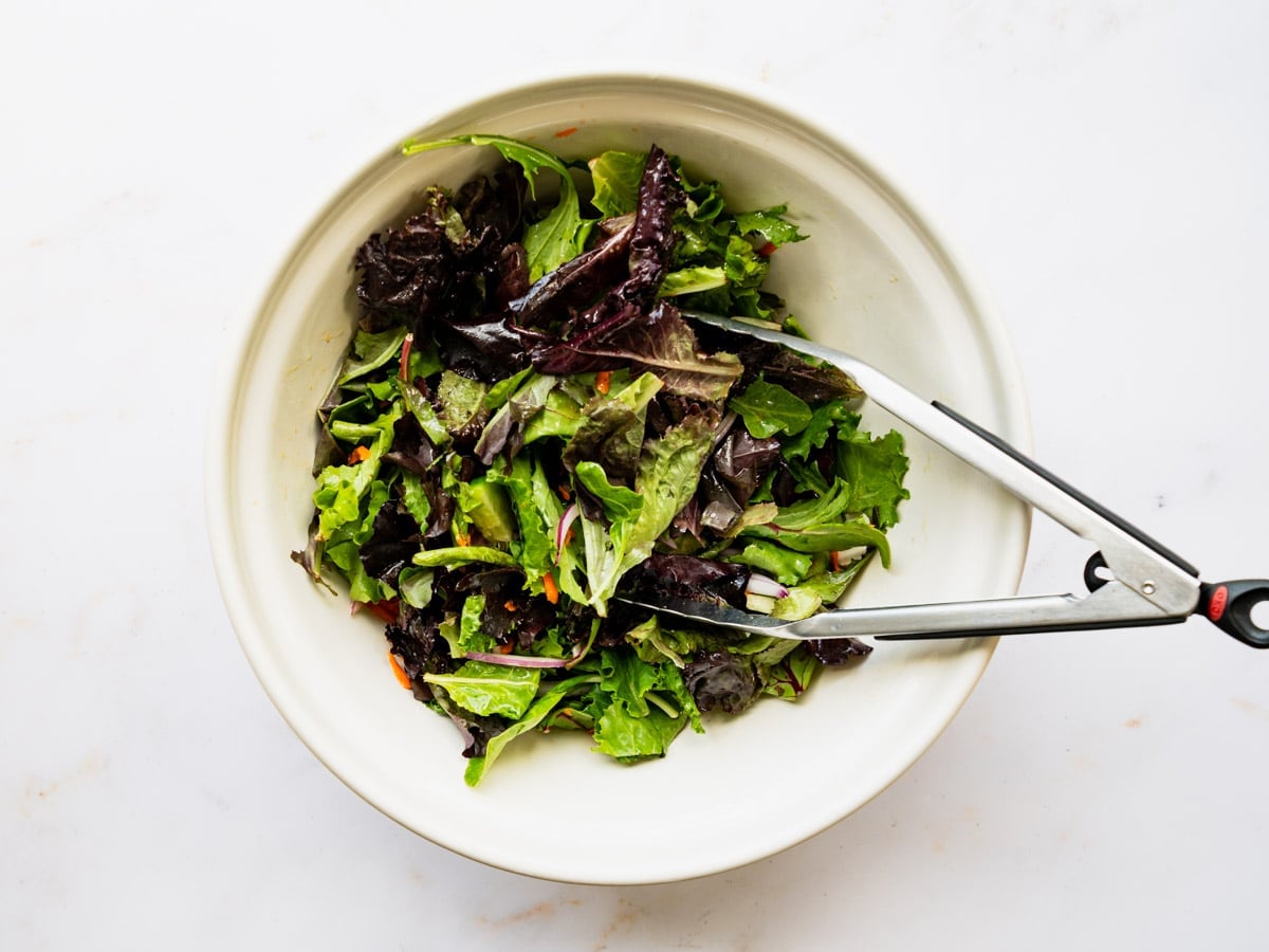 Adding the greens to a large white bowl.