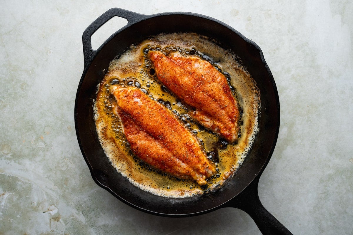 Cooking blackened catfish fillets in a cast iron pan.