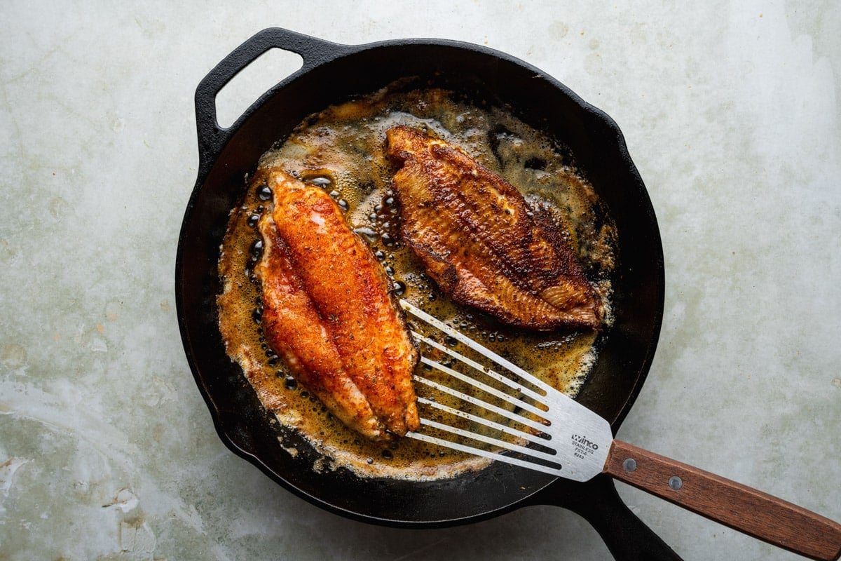 Flipping blackened catfish fillets in a cast iron sklilet.