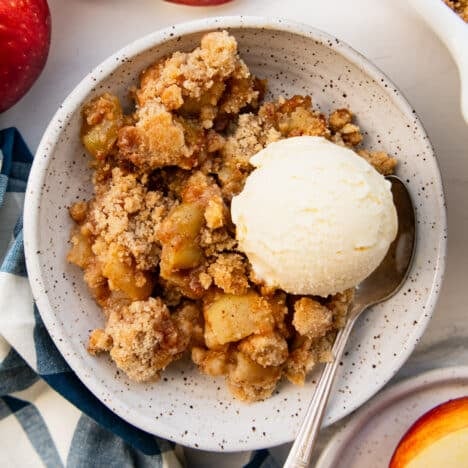 Square overhead shot of a bowl of apple crumble with a scoop of vanilla ice cream on top.