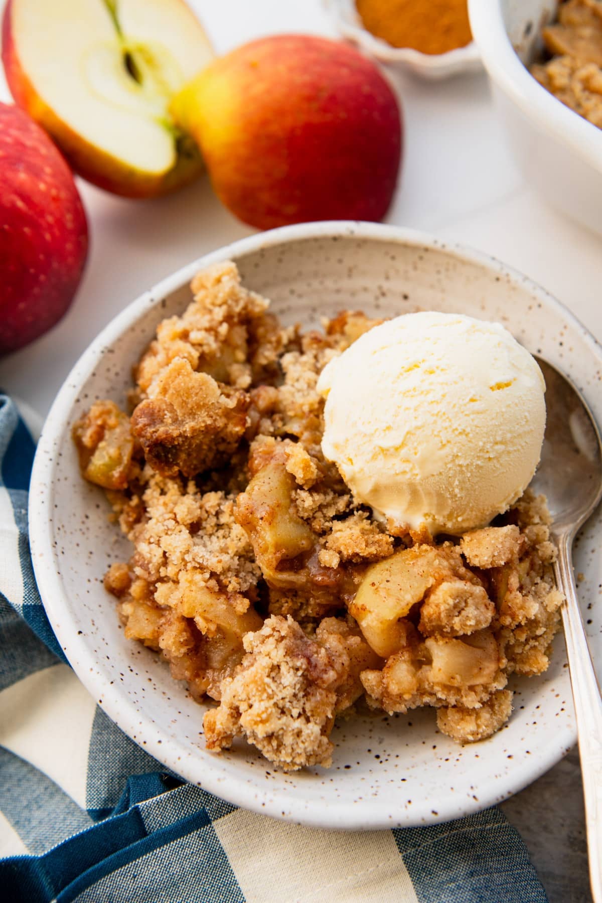 Close up side shot of a bowl of apple crumble with a scoop of vanilla ice cream on top.