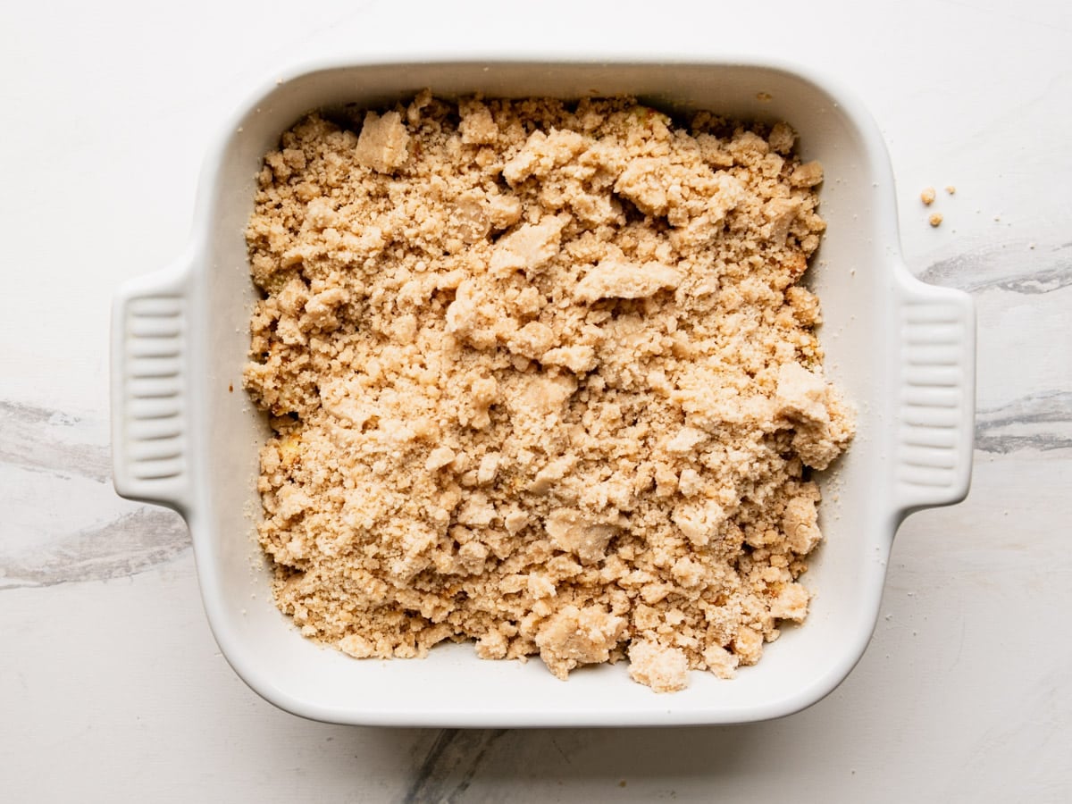 Adding the topping to an apple crumble before it goes in the oven.