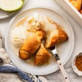 Horizontal overhead shot of two crescent roll apple dumplings on a white plate with a couple scoops of vanilla ice cream.