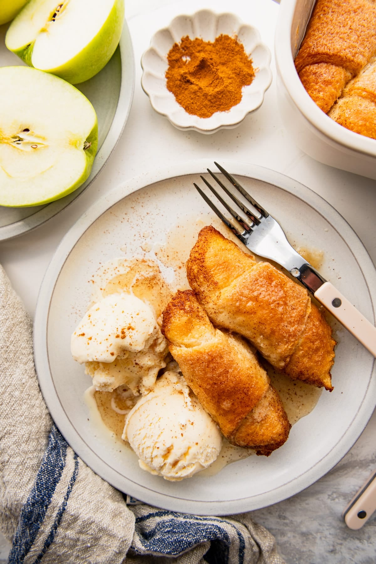 Overhead shot of two crescent roll apple dumplings on a white plate with a couple scoops of vanilla ice cream.