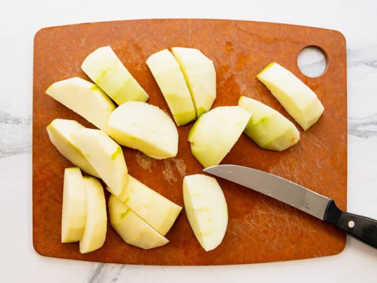 Peeled and sliced Granny Smith apples on a cutting board.