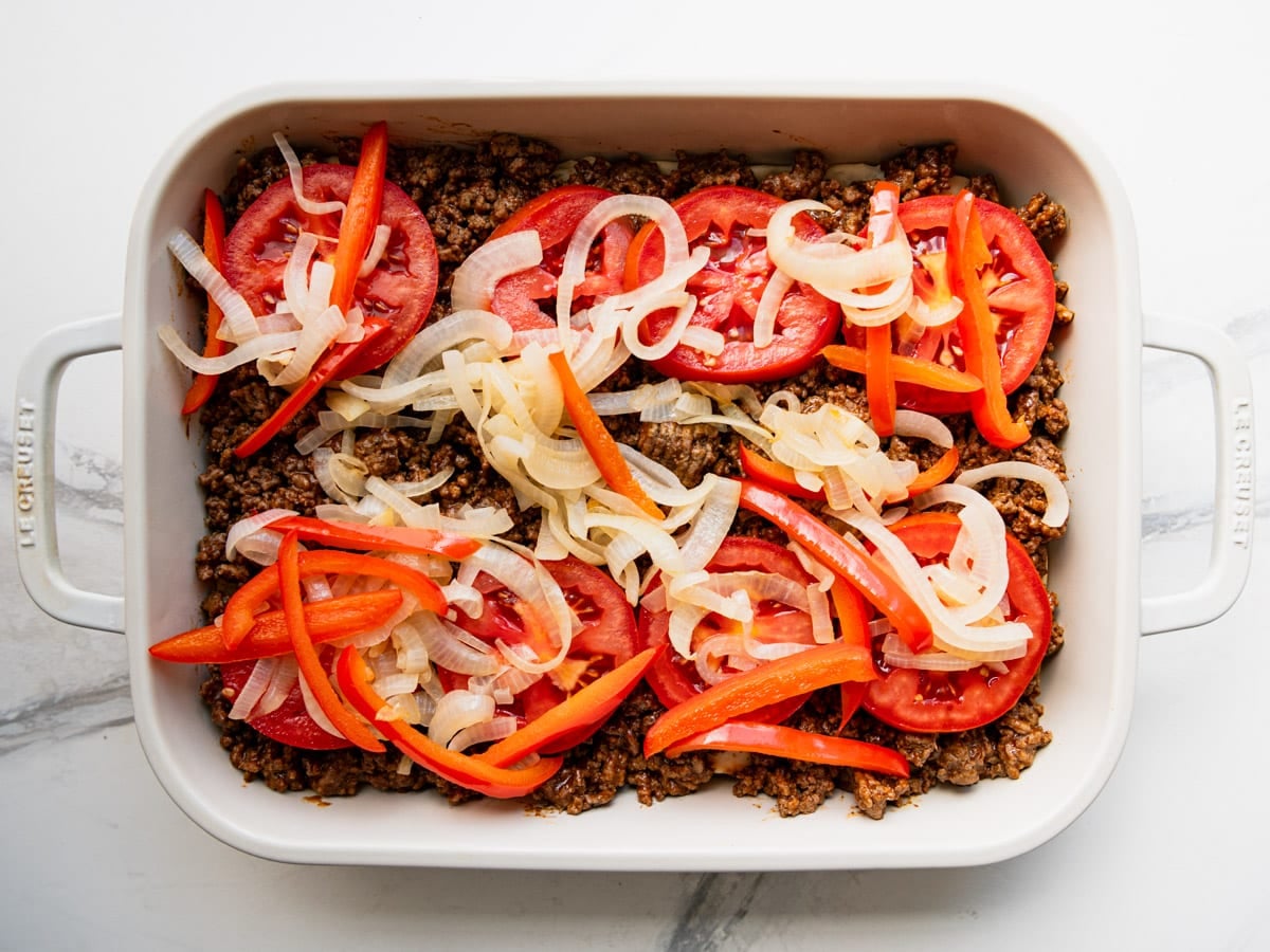 Spreading the peppers and onions in the dish.