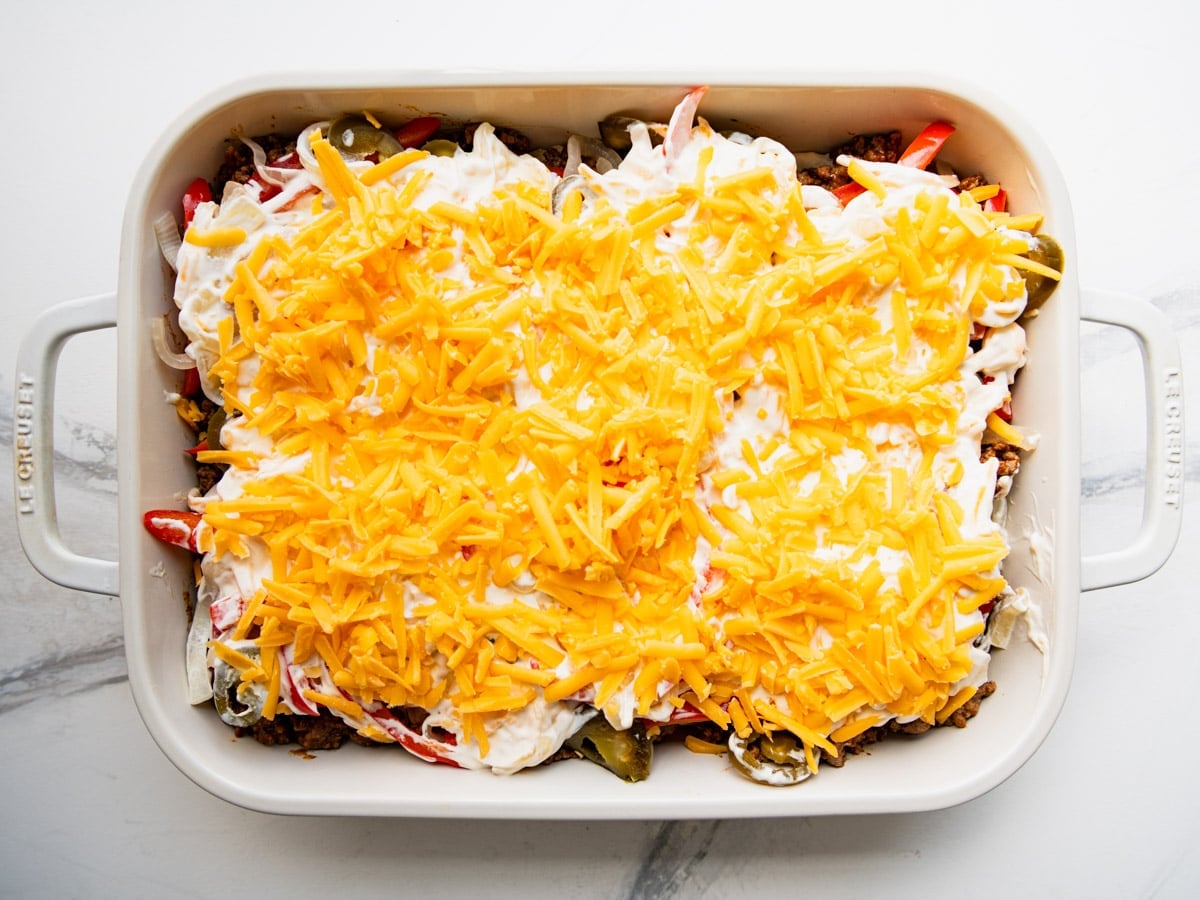 Adding the cheese to the top of a John Wayne casserole before it goes in the oven.