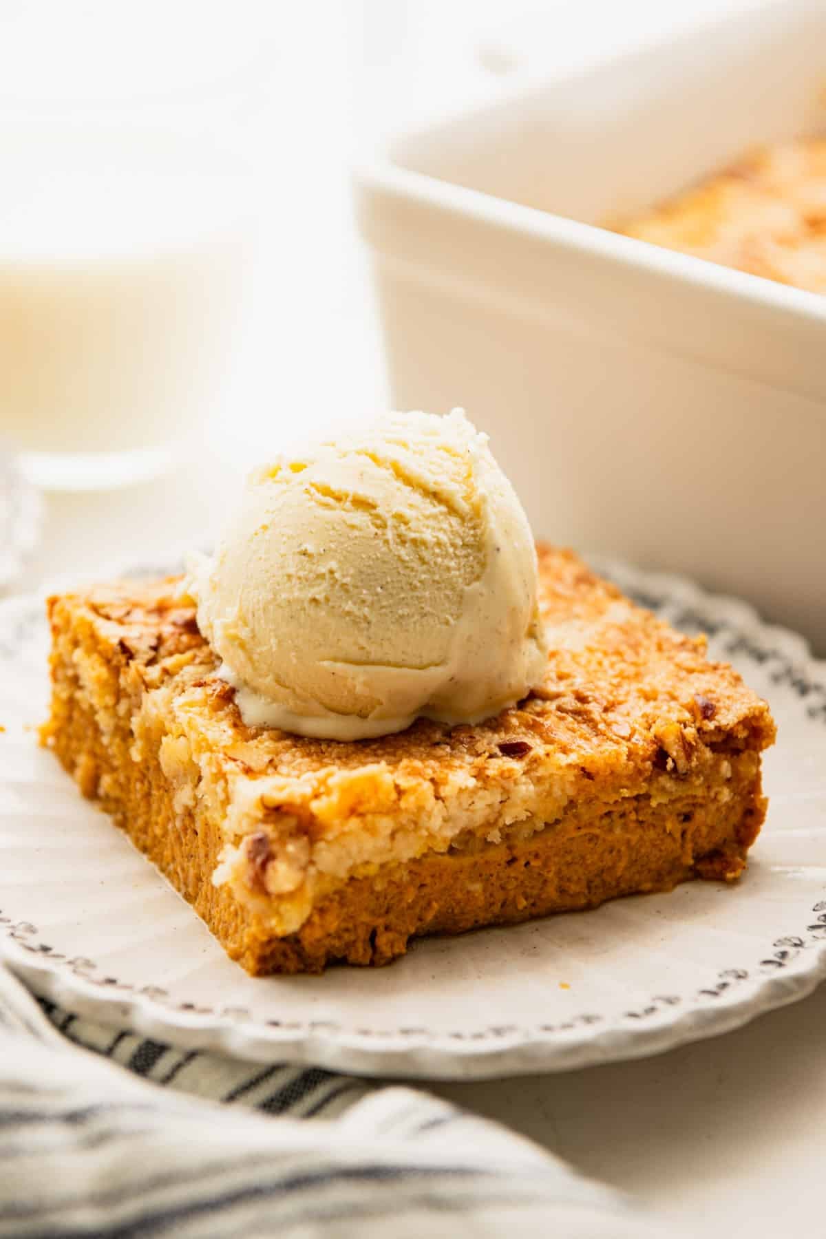 Side shot of a slice of pumpkin dump cake on a plate with vanilla ice cream on top.