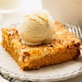 Square side shot of a slice of pumpkin dump cake on a plate with vanilla ice cream on top.
