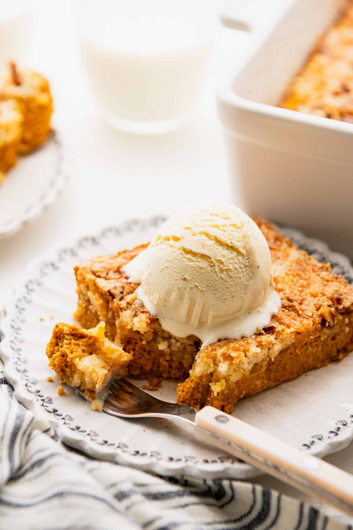 Side shot of a slice of pumpkin dump cake on a plate with vanilla ice cream on top.