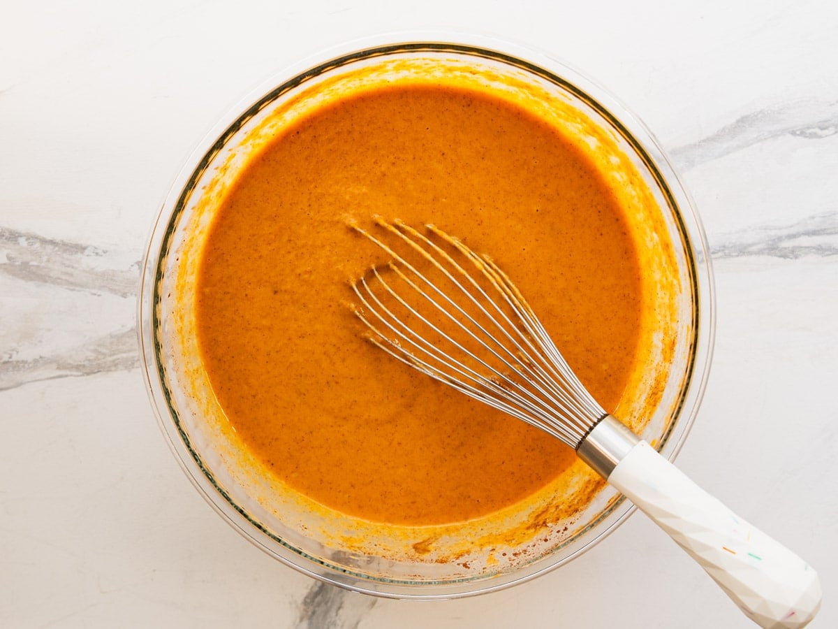 Whisking together a pumpkin pie filling in a glass bowl for a pumpkin dump cake recipe.