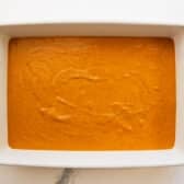 Pumpkin pie filling mixture spread in a white baking dish.