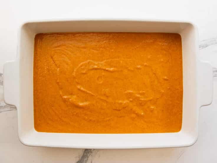 Pumpkin pie filling mixture spread in a white baking dish.