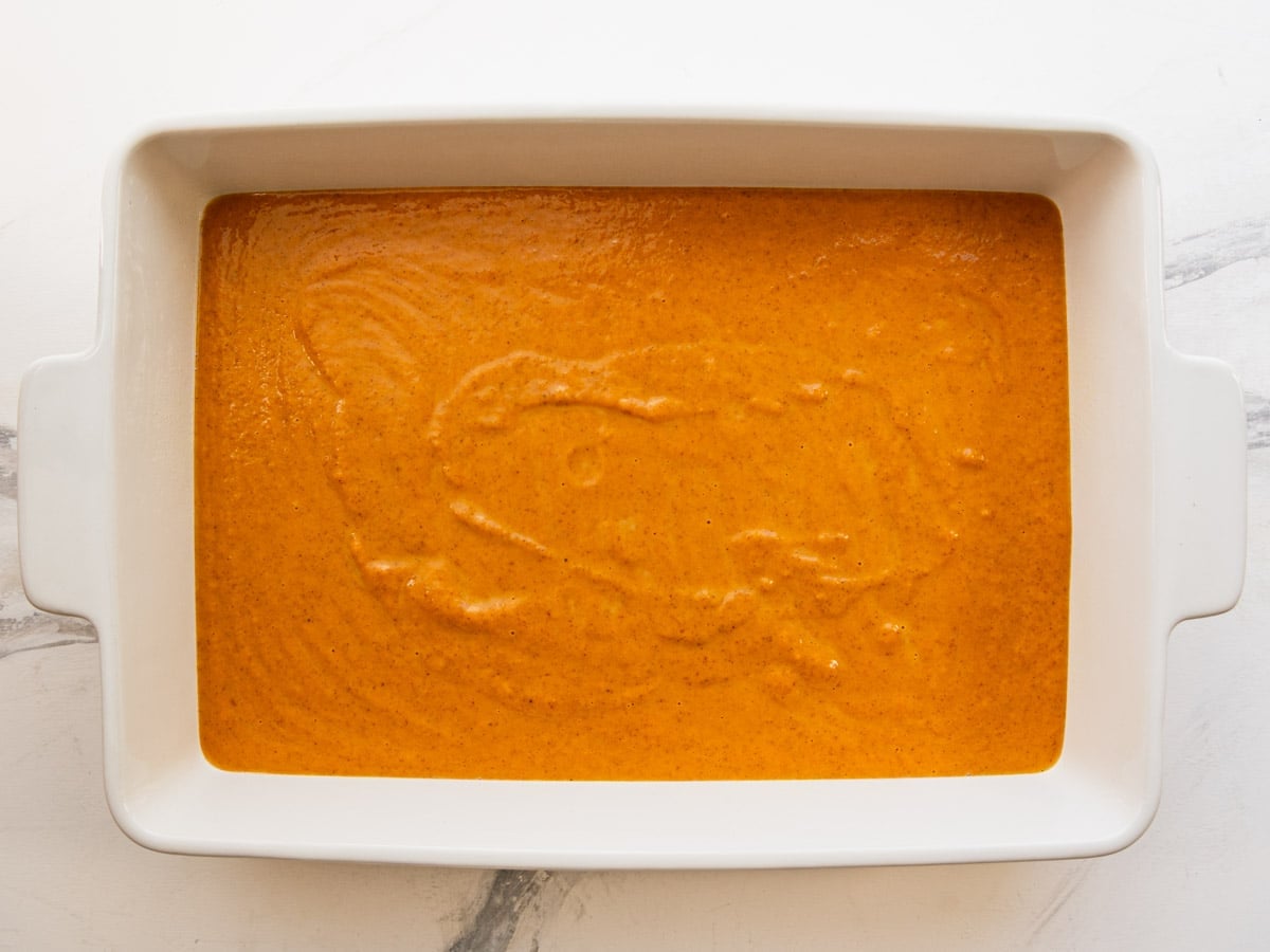 Pumpkin pie filling mixture spread in a white baking dish.
