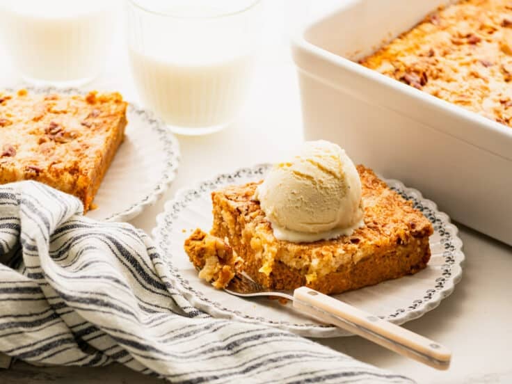 Horizontal side shot of a slice of pumpkin dump cake on a plate with vanilla ice cream on top.