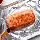 Basting meatloaf with glaze before wrapping it in bacon.