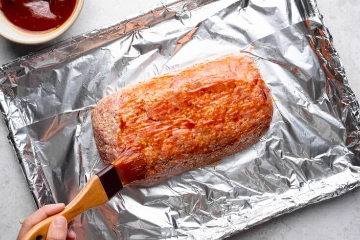 Basting meatloaf with glaze before wrapping it in bacon.