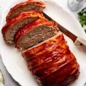 Horizontal overhead shot of a sliced bacon wrapped meatloaf on a white serving platter.