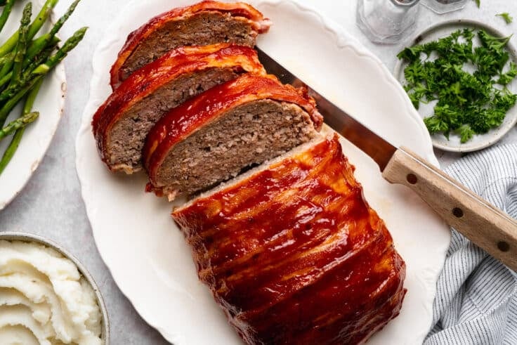 Horizontal overhead shot of a sliced bacon wrapped meatloaf on a white serving platter.