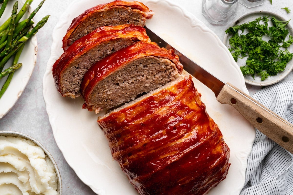 Horizontal overhead shot of a sliced bacon wrapped meatloaf on a white serving platter.