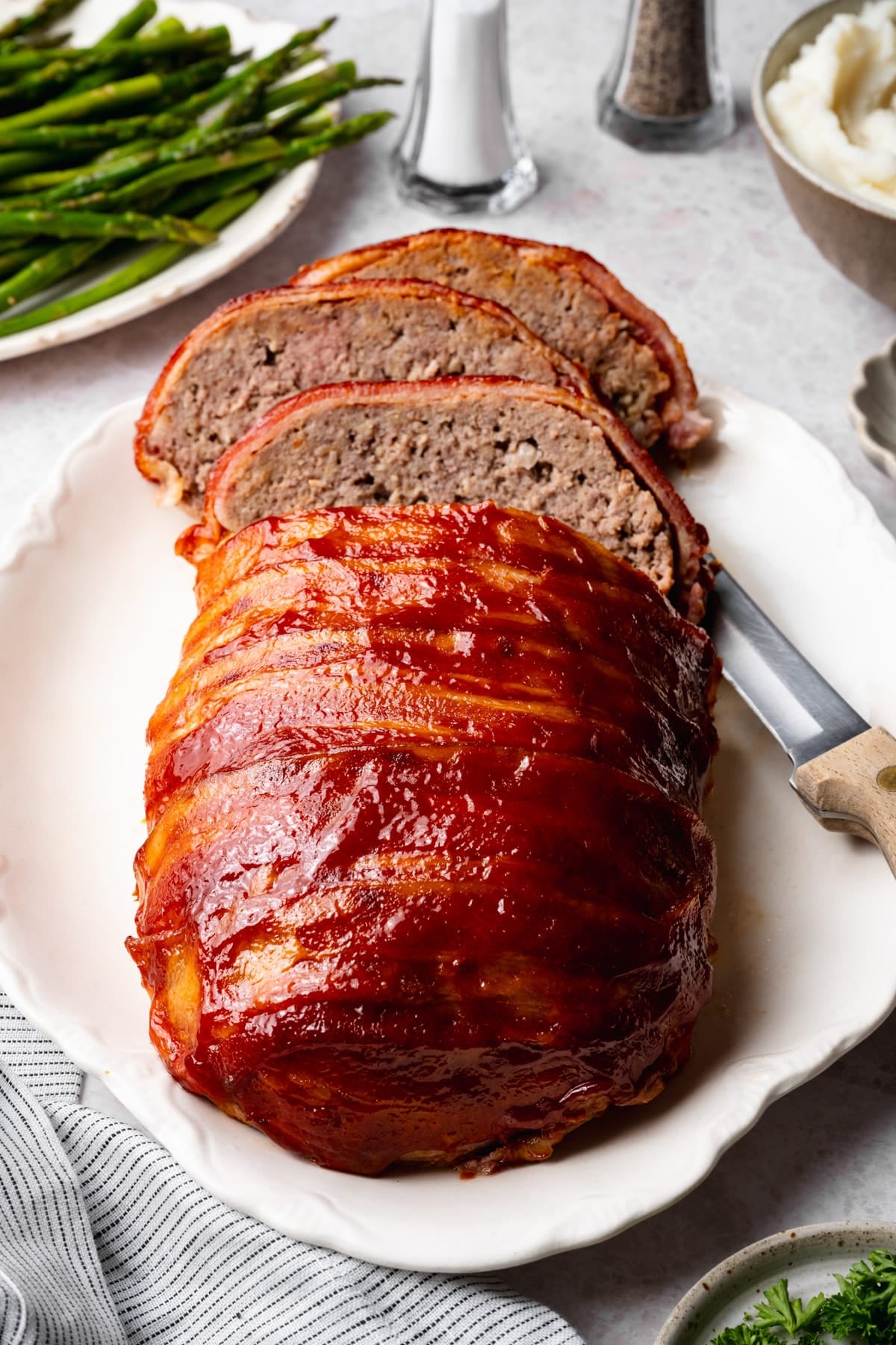 Front shot of a sliced bacon wrapped meatloaf on a white serving platter.