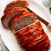 Overhead shot of a sliced bacon wrapped meatloaf on a white serving platter.